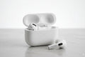 White wireless earbuds with charging case on a light gray surface